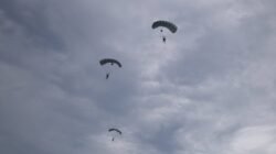 Tiga prajurit Korps Pasukan Gerak Cepat (Korpasgat) melakukan terjun payung di langit Biak dengan latar belakang awan mendung. (Dok. HO/Faktakalbar.id)