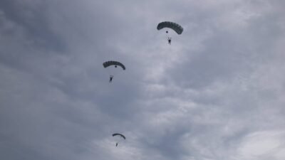 Tiga prajurit Korps Pasukan Gerak Cepat (Korpasgat) melakukan terjun payung di langit Biak dengan latar belakang awan mendung. (Dok. HO/Faktakalbar.id)