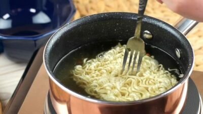 Ilustrasi seseorang sedang menyeduh mi instan yang jika dikonsumsi secara berlebihan dapat memicu berbagai masalah kesehatan jangka panjang.