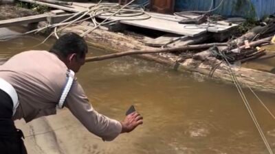 Seorang personel kepolisian berpakaian dinas lengkap sedang melakukan pengecekan dan memotret titik fenomena alam di tepi Sungai Kapuas, Dusun Kubu, Desa Ujung Pandang. (Dok. HO/Faktakalbar.id)