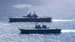 Dua kapal perang militer berlayar berdampingan di lautan lepas, salah satunya adalah kapal serbu amfibi Angkatan Laut Amerika Serikat USS Tripoli (LHA-7). (Dok. DVIDS)