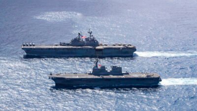 Dua kapal perang militer berlayar berdampingan di lautan lepas, salah satunya adalah kapal serbu amfibi Angkatan Laut Amerika Serikat USS Tripoli (LHA-7). (Dok. DVIDS)