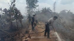 Petugas kepolisian dari Polres Mempawah dan Polsek Mempawah Timur saat berjibaku menyemprotkan air untuk memadamkan api karhutla yang membakar lapisan gambut di bawah badan jalan.