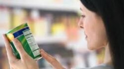 Seorang perempuan muda sedang meneliti label informasi gizi pada kemasan minuman ringan sebelum memutuskan untuk membelinya di swalayan.