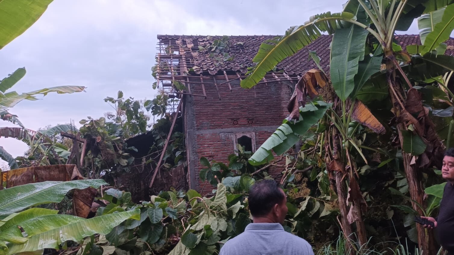 Tim gabungan dari BPBD dan warga sekitar bergotong royong membersihkan material pohon tumbang yang menimpa bangunan akibat terjangan angin kencang.