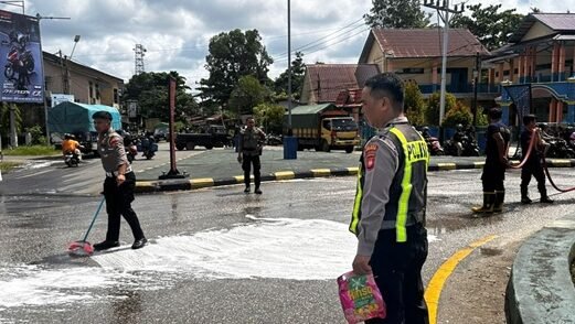 Personel gabungan dari kepolisian dan pemadam kebakaran saat membersihkan permukaan jalan aspal dari genangan bahan bakar solar di kawasan Tugu PKK.
