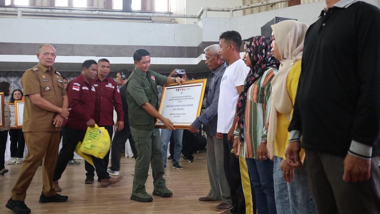 Kepala BNPB Letjen TNI Suharyanto (baju rompi hijau) menyerahkan dana stimulan perbaikan rumah secara simbolis kepada warga terdampak bencana hidrometeorologi basah akibat Siklon Senyar di Gedung GOR Pandan, Sibolga, Tapanuli Tengah, Selasa (21/4).